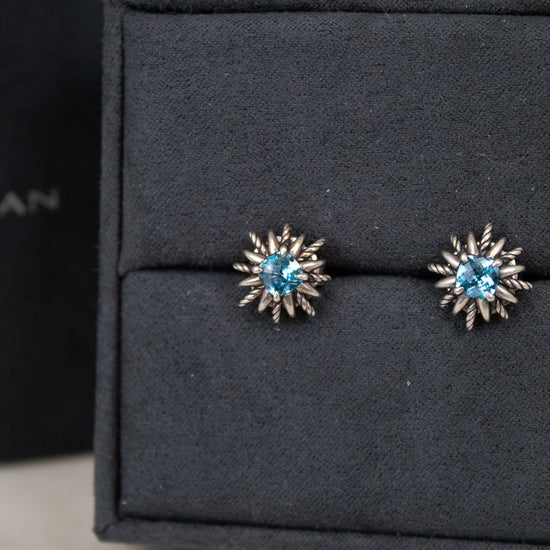 Pair of starburst-shaped earrings with blue gemstones on a black jewelry box.