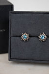 Pair of starburst-shaped earrings with blue gemstones on a black jewelry box.