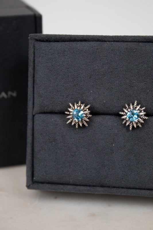 Pair of starburst-shaped earrings with blue gemstones on a black jewelry box.