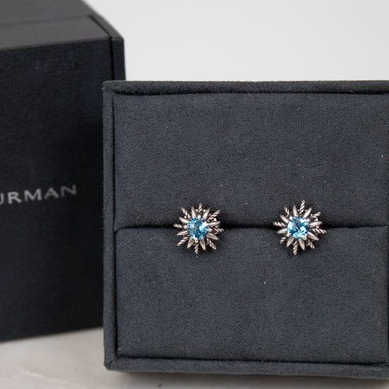 Pair of starburst earrings with blue gemstones in center on a black jewelry box.