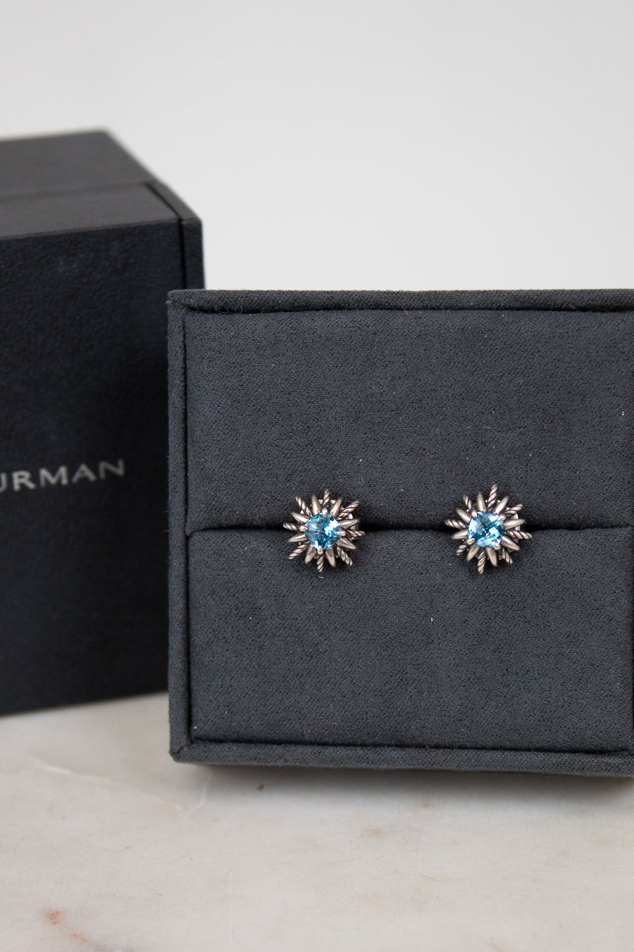 Pair of starburst earrings with blue gemstones in center on a black jewelry box.