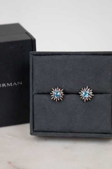 Pair of starburst earrings with blue gemstones in center on a black jewelry box.