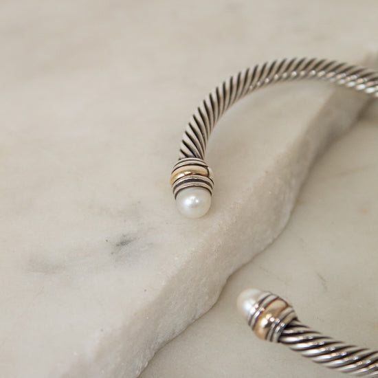 Silver bracelet with a pearl detail on the ends on a marble surface