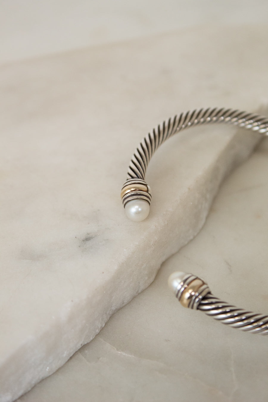 Silver bracelet with a pearl detail on the ends on a marble surface