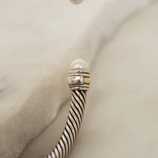 Silver bracelet with striped cable design with pearl details on a light background