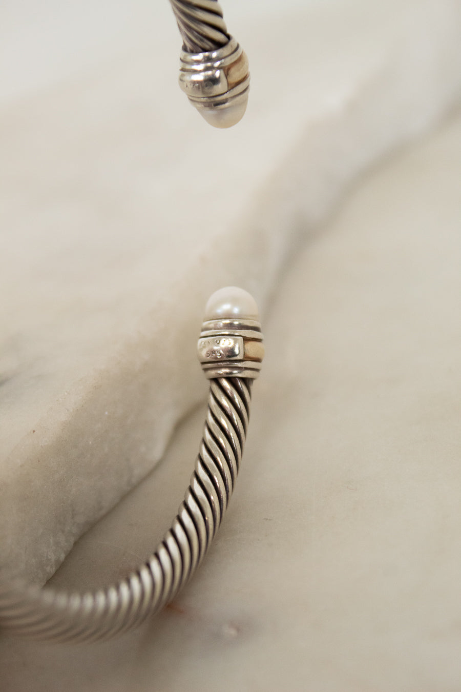 Silver bracelet with striped cable design with pearl details on a light background