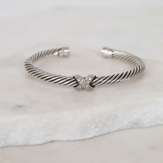 Silver bracelet with a gold and diamond 'X' station design on a marble surface