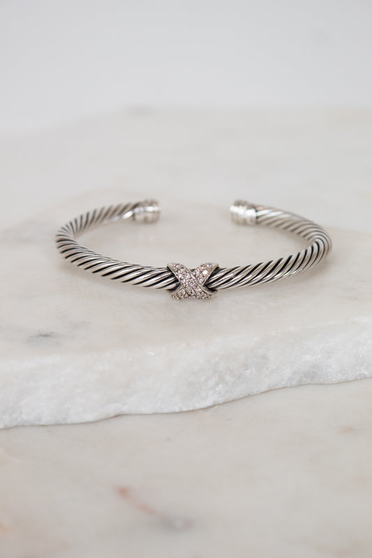 Silver bracelet with a gold and diamond 'X' station design on a marble surface