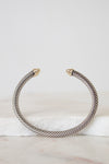 A twisted cable-style cuff bracelet in silver-tone metal with small gold-toned tips, displayed on a white marble surface against a light gray background.