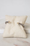 A silver twisted cable cuff bracelet with gold details displayed on a small beige fabric jewelry pillow over a white marble surface.