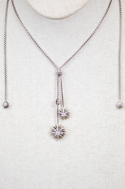 Silver necklace with starburst pendants on a light gray background