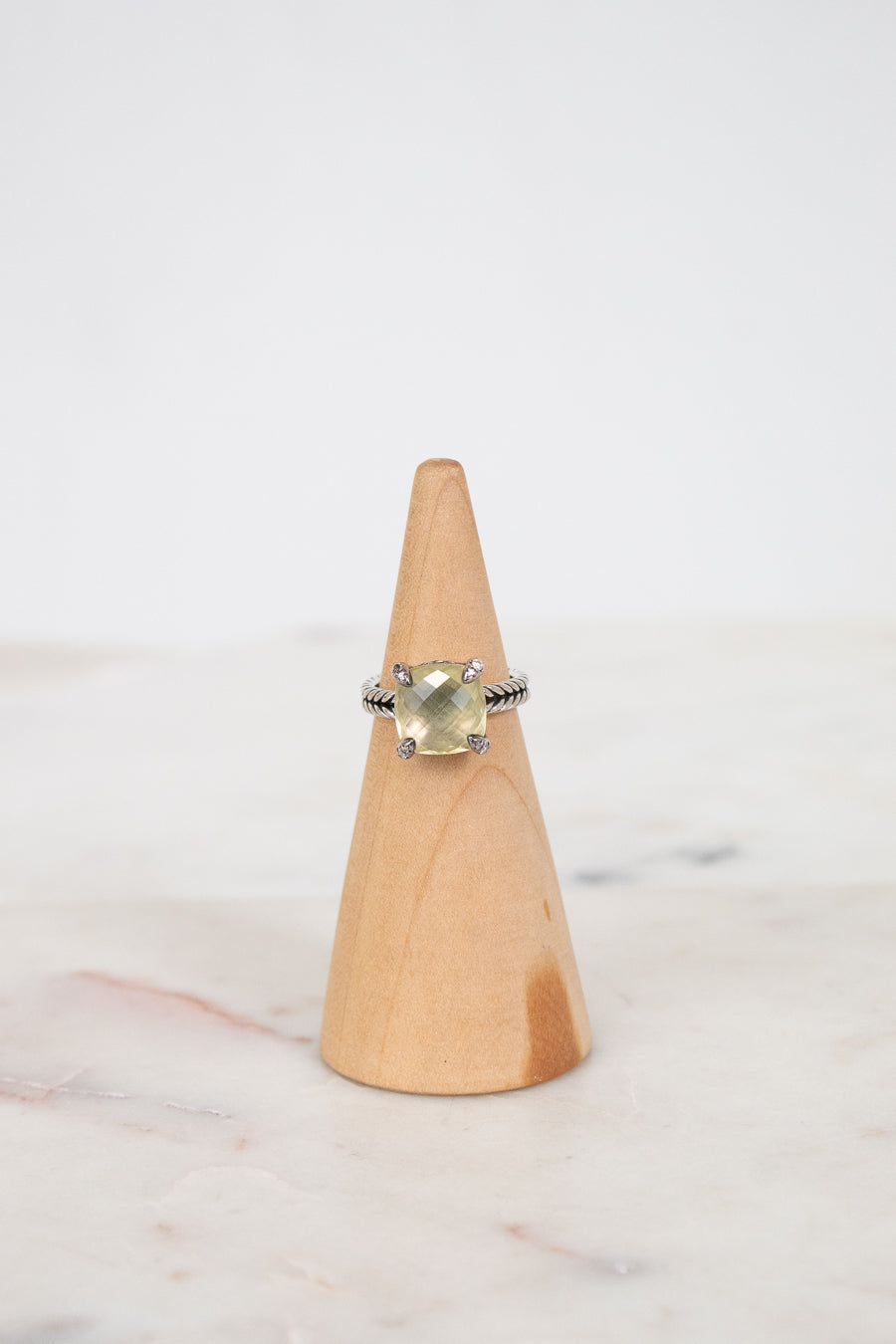 Ring with a yellow gemstone on a wooden cone against a white background
