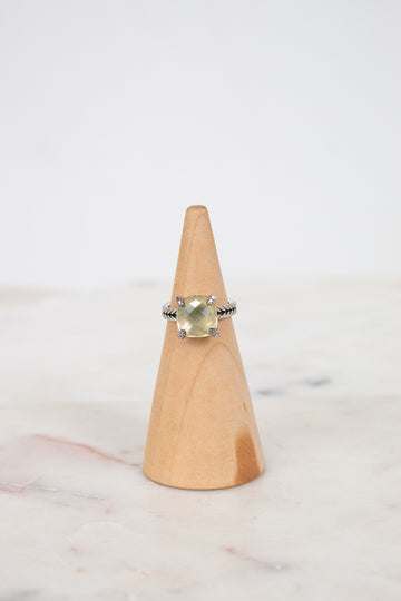 Ring with a yellow gemstone on a wooden cone against a white background