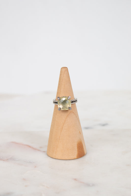 Ring with a yellow gemstone on a wooden cone against a white background