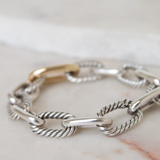 A gold and silver-toned cable link chain bracelet displayed across a light marble surface. 
