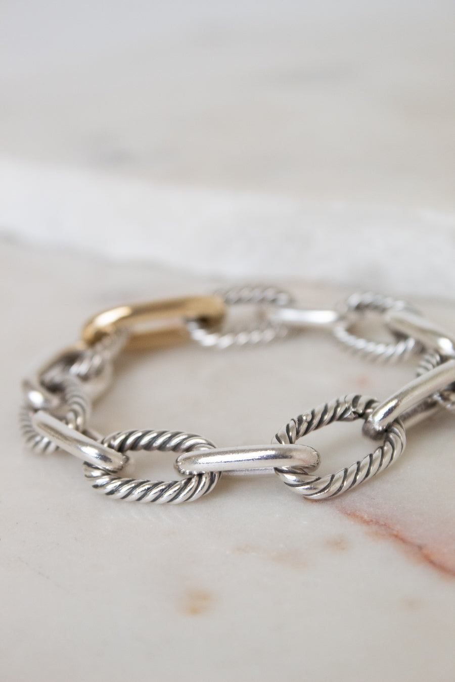 A gold and silver-toned cable link chain bracelet displayed across a light marble surface. 