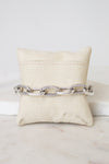 A silver-toned cable link chain bracelet displayed across a cream fabric jewelry pillow on a light marble surface.