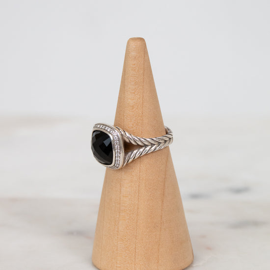 Silver ring with a black gemstone on a wooden cone against a light background