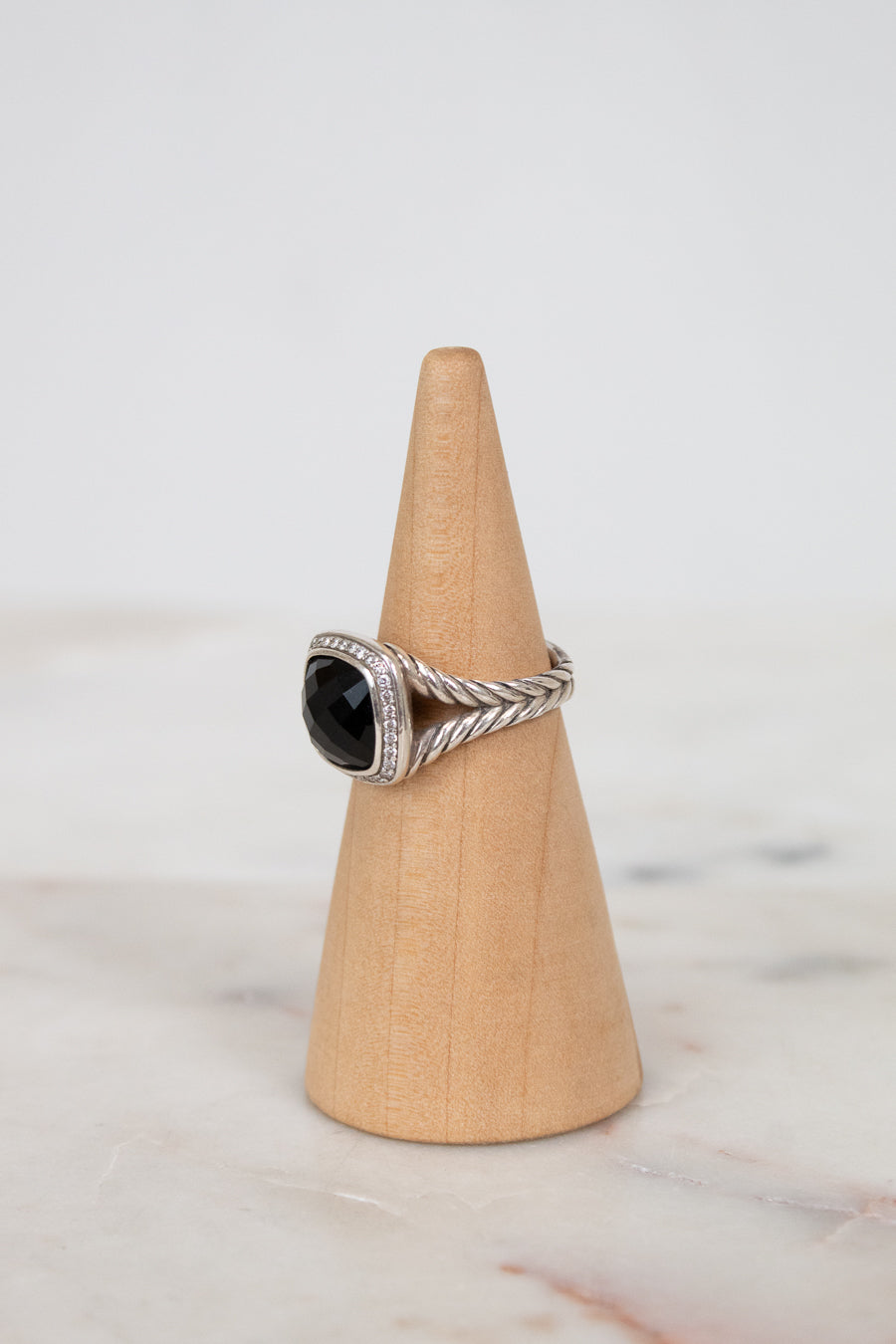 Silver ring with a black gemstone on a wooden cone against a light background