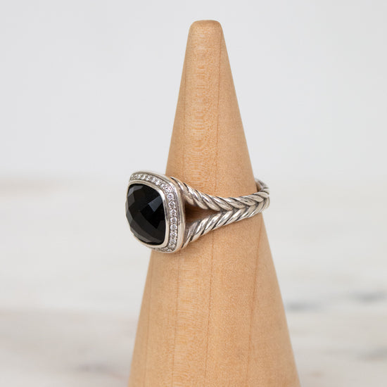 Silver ring with a black gemstone on a wooden cone against a white background