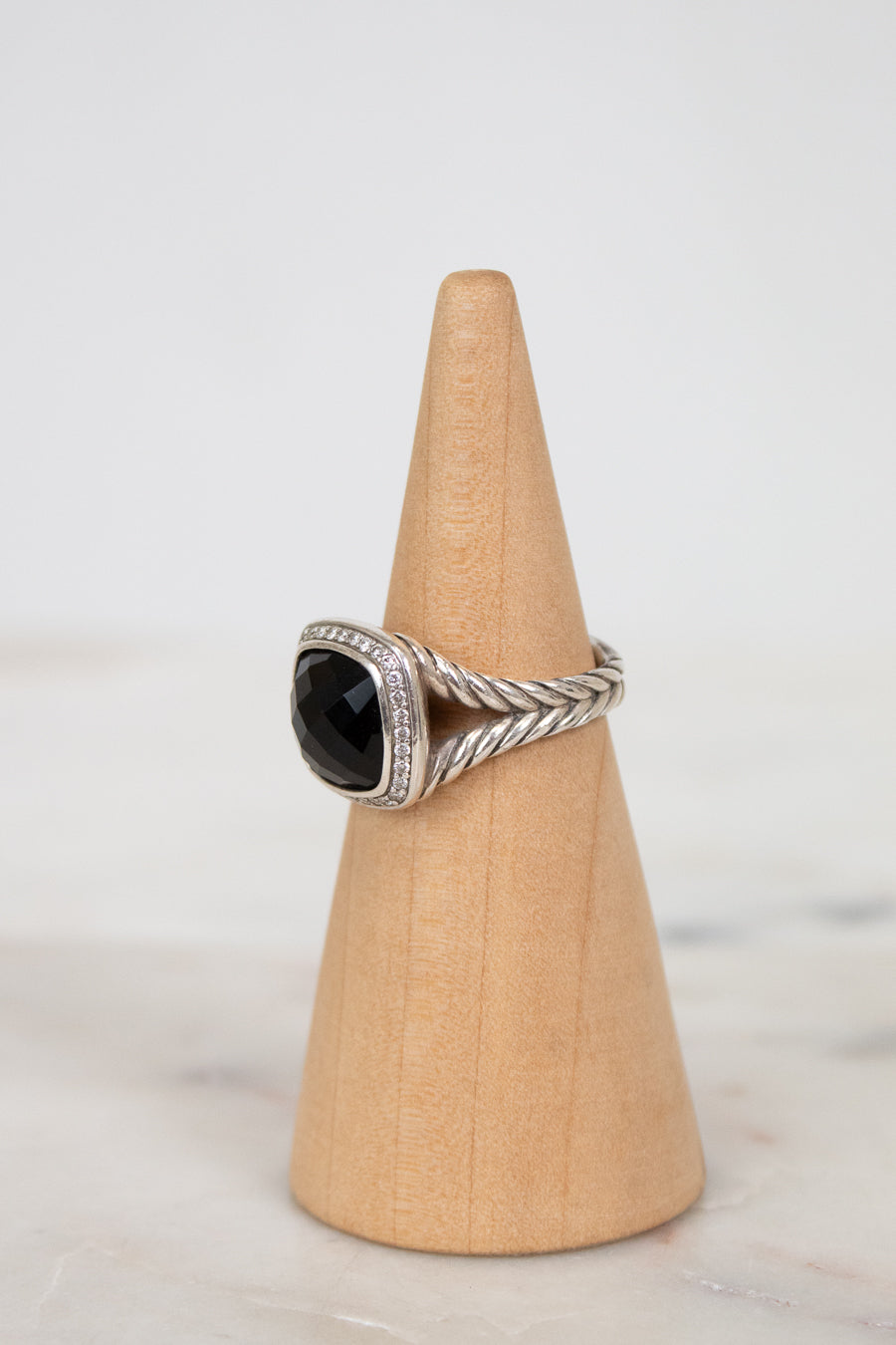 Silver ring with a black gemstone on a wooden cone against a white background