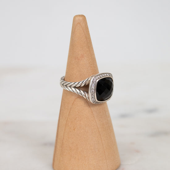 Silver ring with a black stone on a wooden cone against a light background