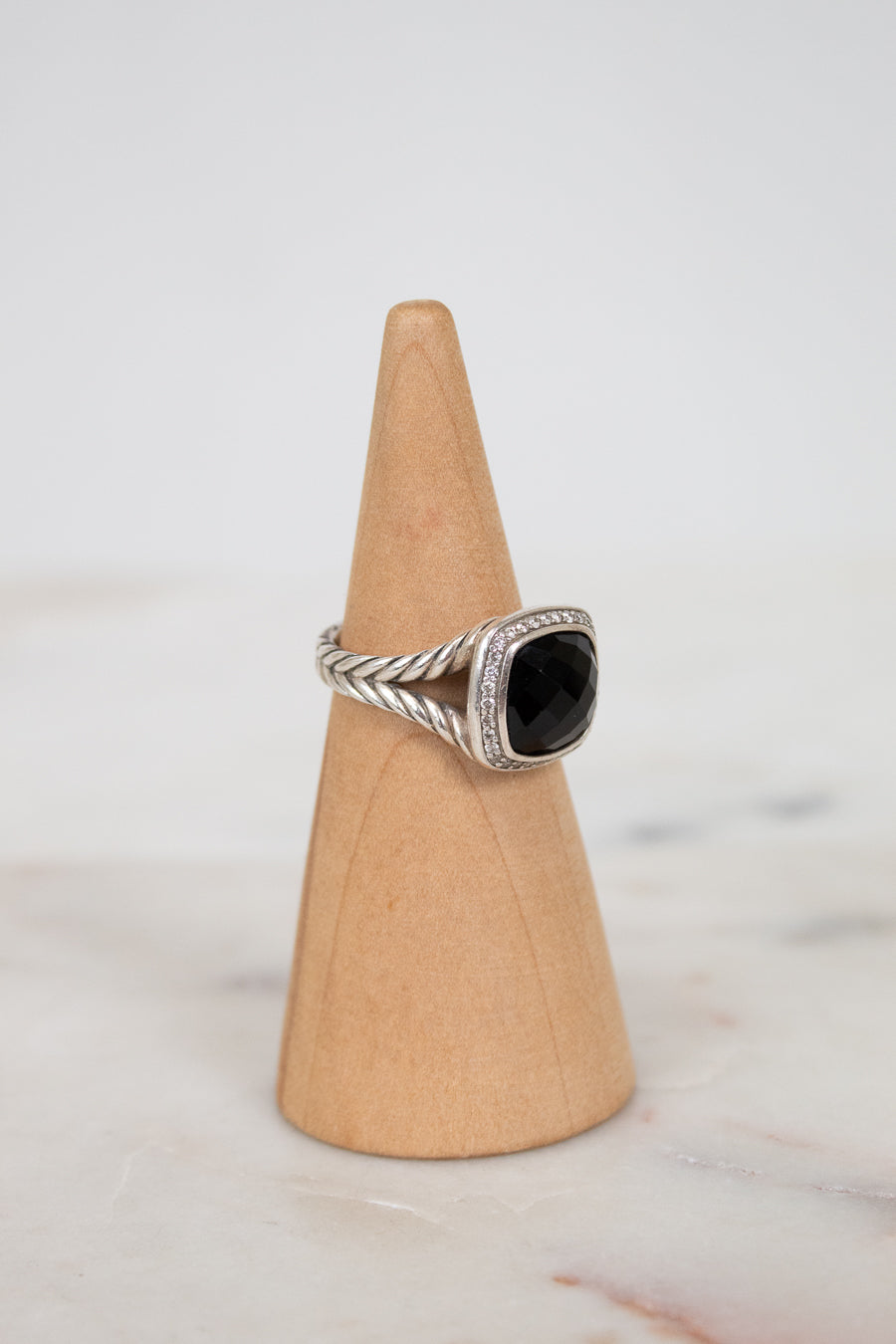 Silver ring with a black stone on a wooden cone against a light background