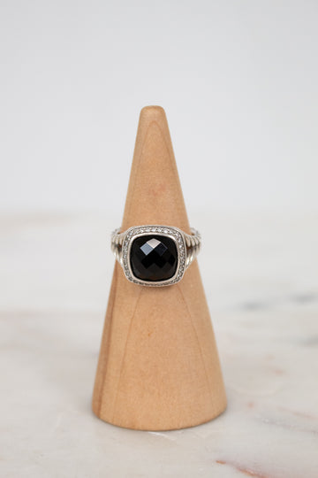 Ring with a black gemstone on a wooden cone against a light background
