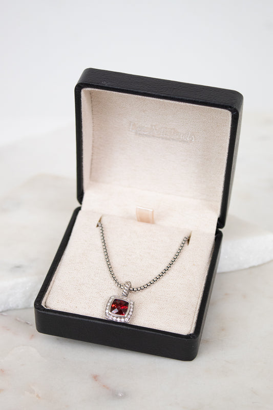 Necklace with a red gemstone in a black jewelry box on a marble surface