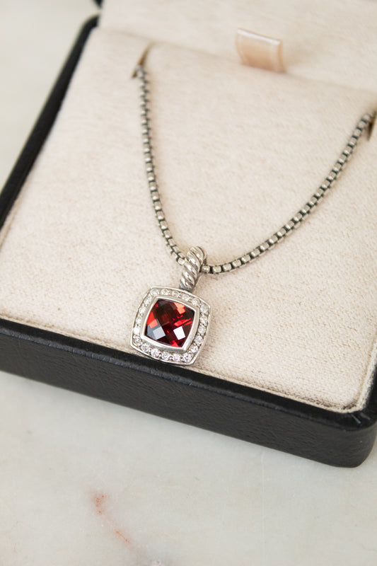 Silver necklace with a red gemstone pendant on a display box.