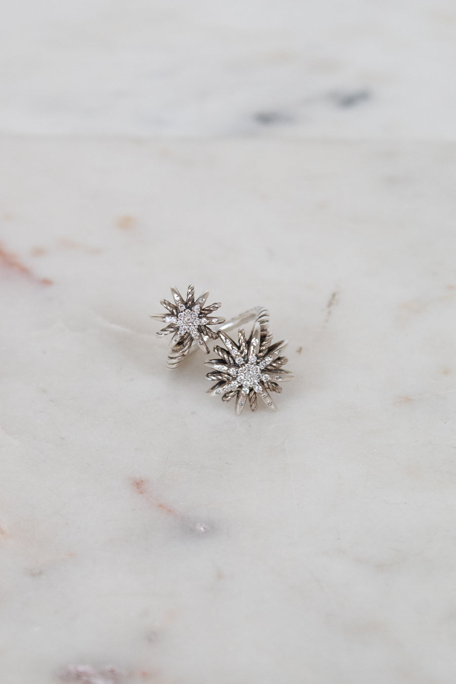 Silver ring with two starburst designs on a marble surface