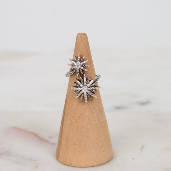 Silver ring with starburst shape design on a wooden ring stand against a marble background