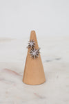 Silver ring with starburst shape design on a wooden ring stand against a marble background