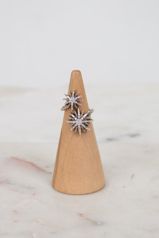 Silver ring with starburst shape design on a wooden ring stand against a marble background