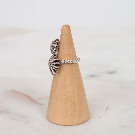 Silver ring with a textured starburst design on a wooden ring stand against a marble background