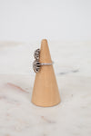Silver ring with a textured starburst design on a wooden ring stand against a marble background