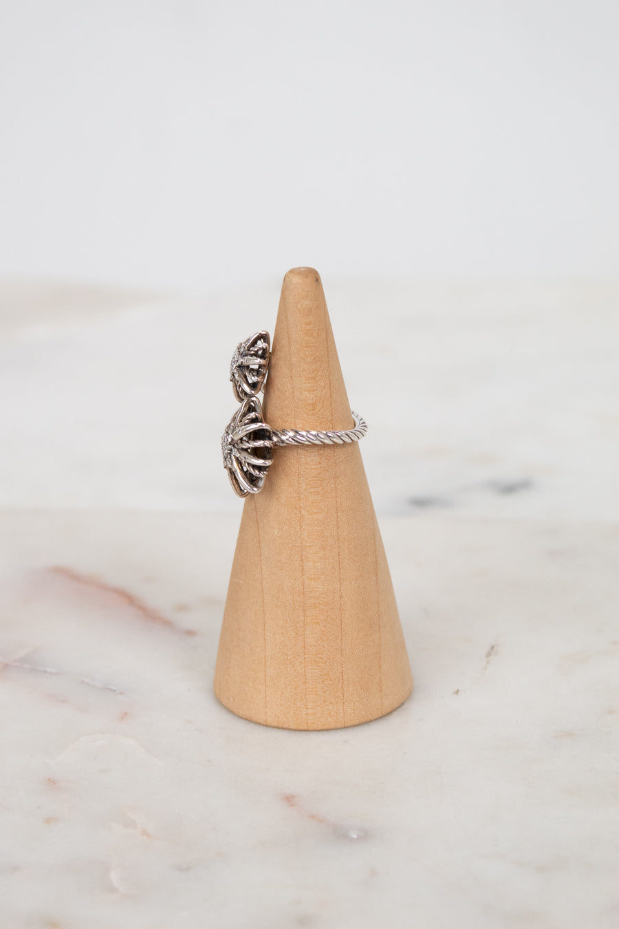 Silver ring with a textured starburst design on a wooden ring stand against a marble background