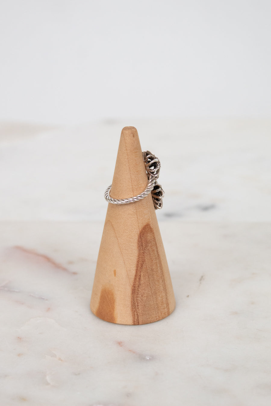 Silver ring on a wooden ring stand against a marble background