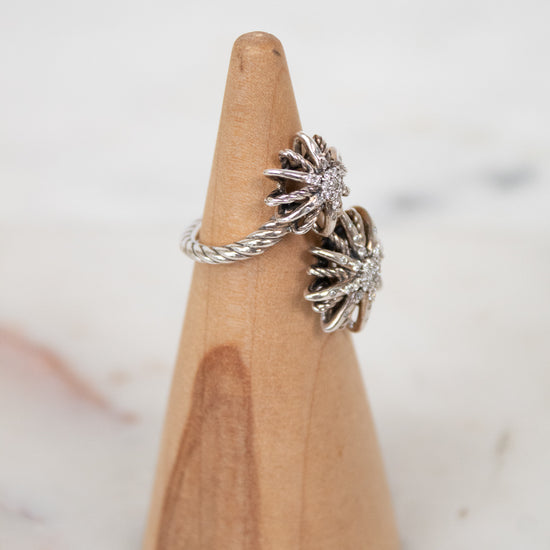 Silver ring with starburst design on a wooden ring stand against a light background