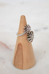 Silver ring with starburst design on a wooden ring stand against a light background