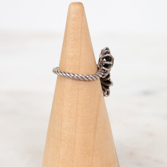 Silver ring with a unique design on a wooden cone against a white background