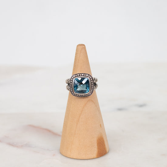 Silver ring with a blue gemstone on a wooden cone against a marble background