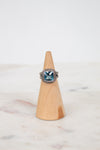 Silver ring with a blue gemstone on a wooden cone against a marble background
