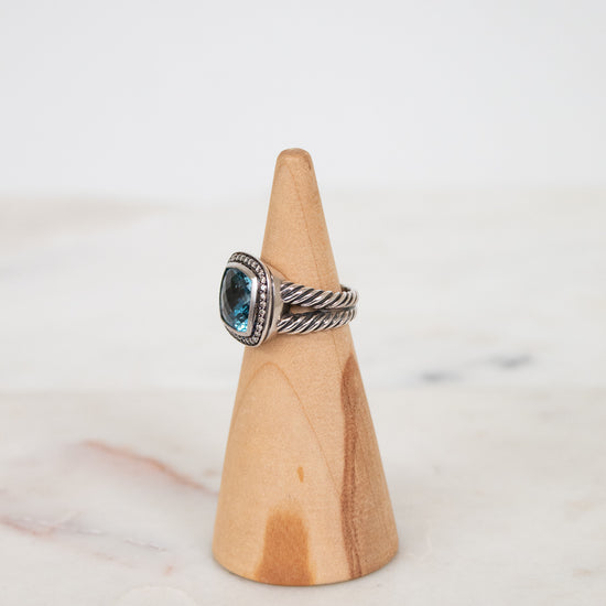 Silver ring with a blue gemstone on a wooden cone against a white background