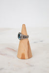 Silver ring with a blue gemstone on a wooden cone against a white background