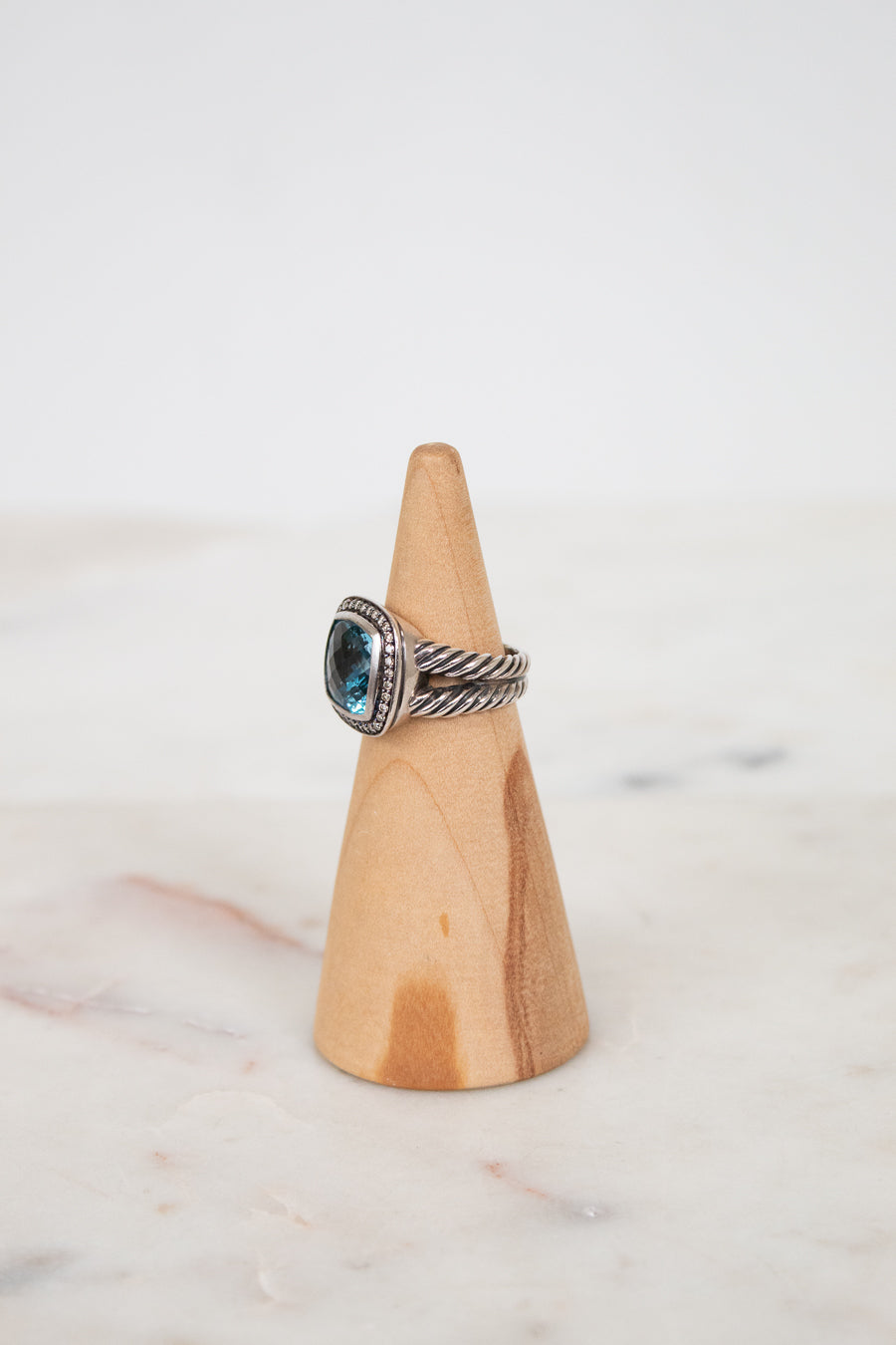 Silver ring with a blue gemstone on a wooden cone against a white background
