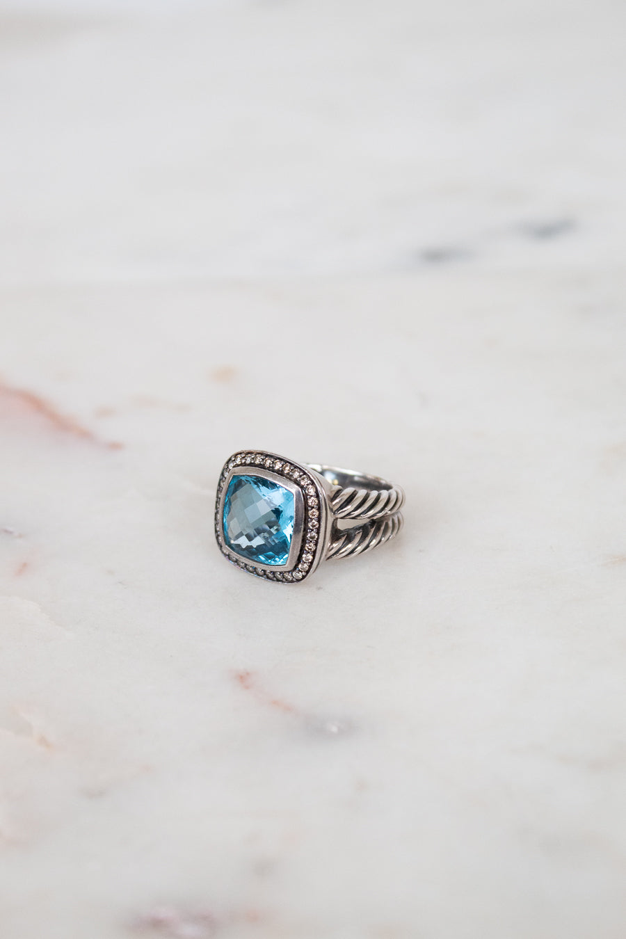 Silver ring with a blue gemstone on a marble surface