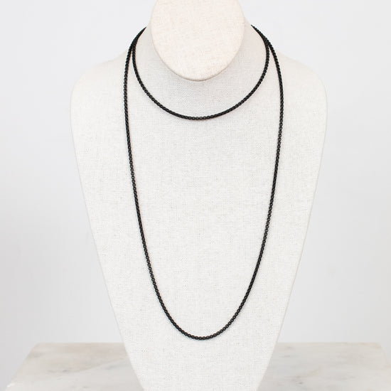 Black necklace on a white mannequin bust against a light gray background