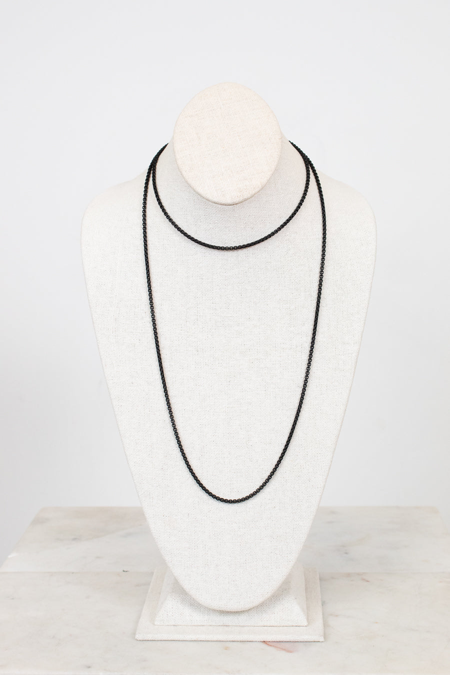Black necklace on a white mannequin bust against a light gray background