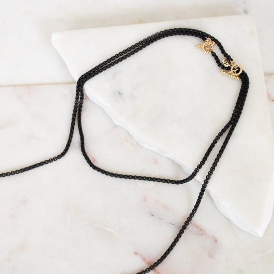 Black chain necklace with a gold clasp on a marble surface